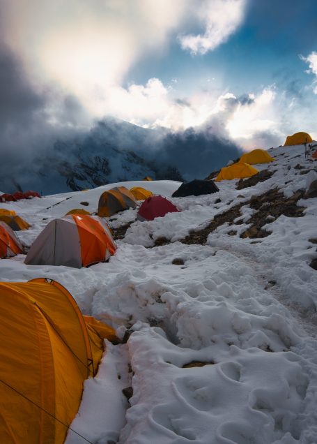 Zeltlager in schneebedecktem Gebirge unter dramatischem Himmel.