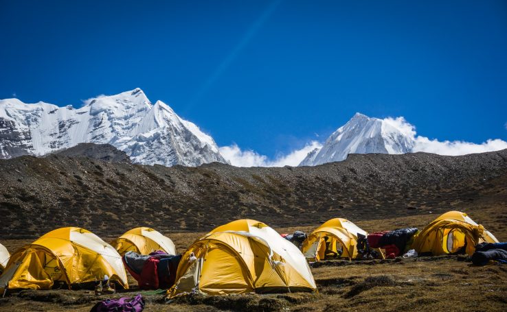 Gelbe Zelte in einer Berglandschaft mit schneebedeckten Gipfeln im Hintergrund.
