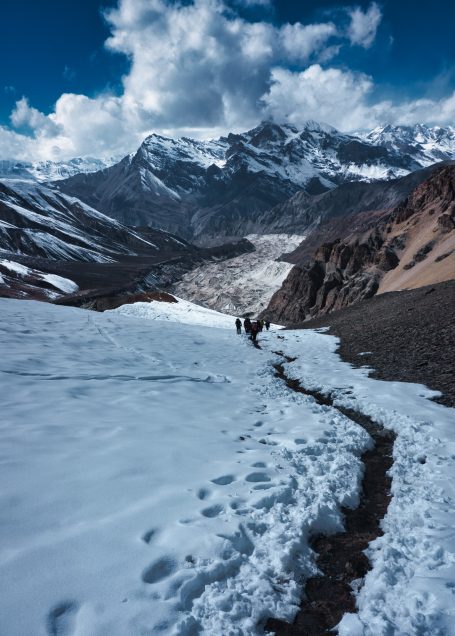 Schneebedeckter Pfad in den Bergen mit Wanderern und majestätischen Gipfeln im Hintergrund.