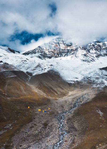 Schneebedeckte Berge mit einem Gletscher und einem kleinen Camp in der Ebene.