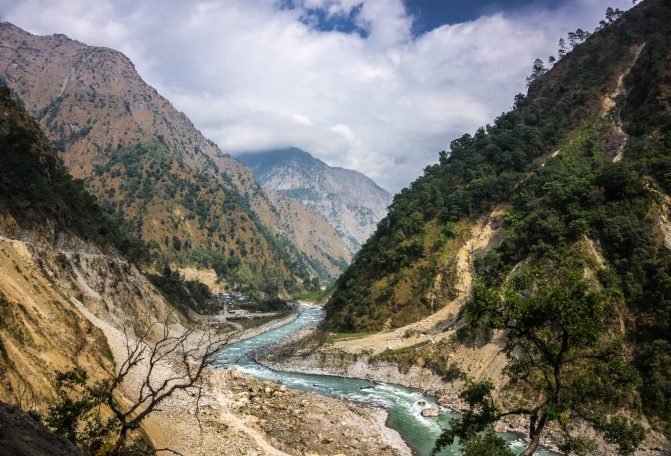 Eine schmale Schlucht mit einem glitzernden Fluss, umgeben von hohen Bergen und Bäumen.