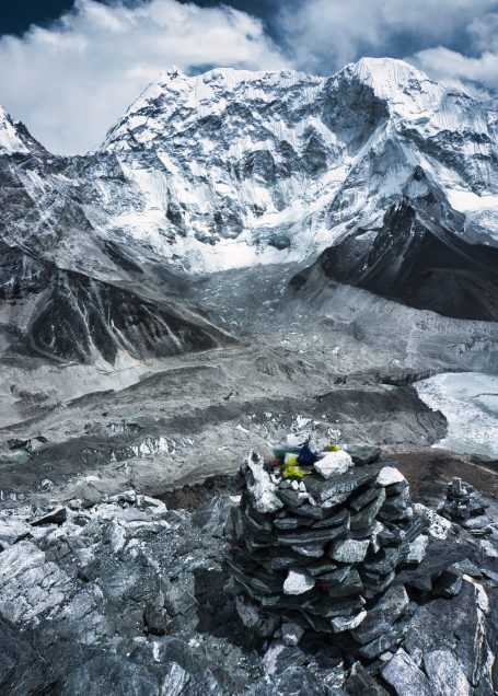 Hochgebirgslandschaft mit schneebedeckten Gipfeln und einem Steinhaufen im Vordergrund.