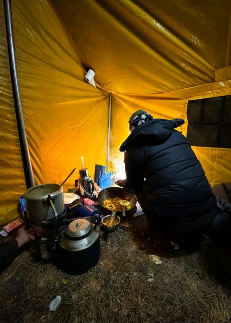 Person kocht in einem Zelt mit gelber Innenausstattung und mehreren Kochutensilien.