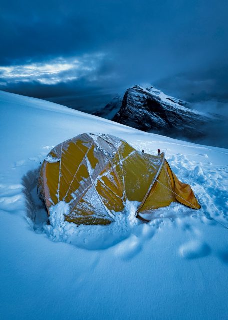 Zelt in einem verschneiten Gebirge, umgeben von Schnee und grauem Himmel.