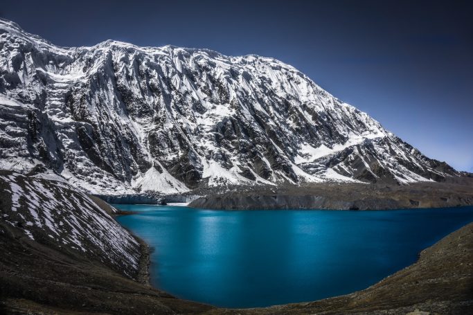 Schneebedeckte Berge umgeben einen türkisfarbenen See.