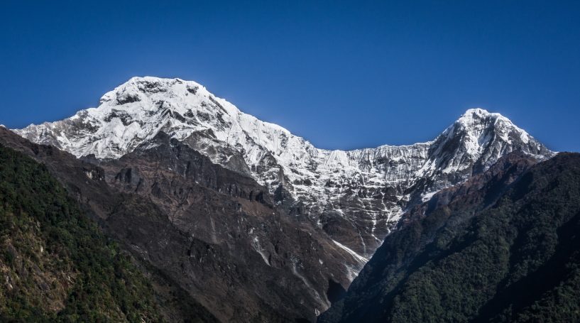 Schneebedeckte Berge unter klarem blauen Himmel, umgeben von dunklen Tälern.