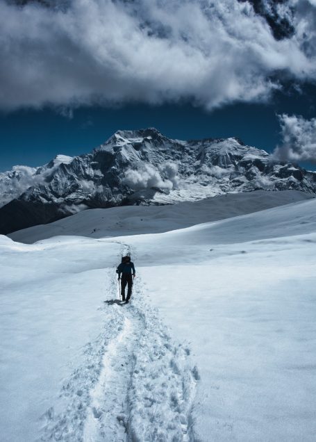 Ein Wanderer geht durch eine schneebedeckte Landschaft mit Bergen im Hintergrund.