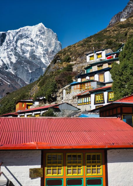 Bunte Häuser in den Bergen mit schneebedeckten Gipfeln im Hintergrund.