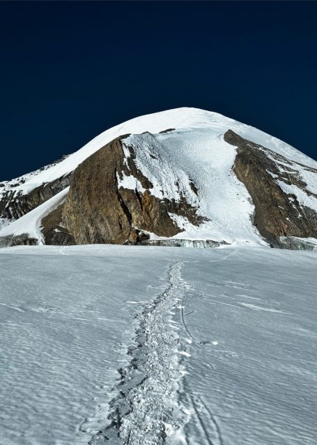 Schneebedeckter Berg unter blauem Himmel mit Spuren im Schnee.
