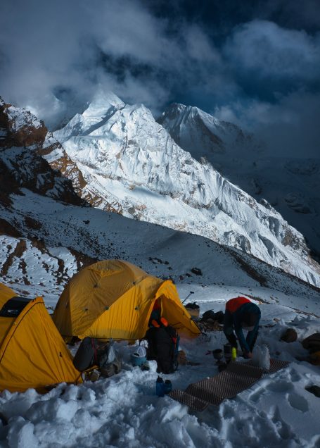 Zelte im Schnee vor einem hohen, schneebedeckten Berg unter bewölktem Himmel.