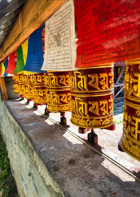 Bunte Gebetsmühlen in einer Reihe, gehängt unter bunten Flaggen.