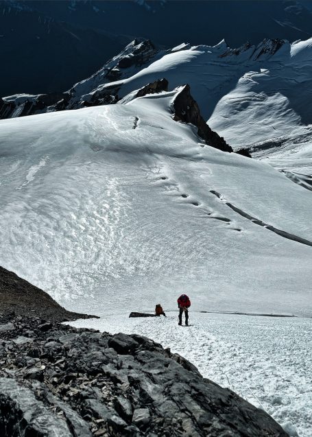 Zwei Wanderer auf einem verschneiten Berggipfel mit gewelltem Terrain im Hintergrund.
