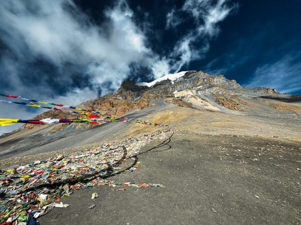 Berglandschaft mit bunten Gebetsfahnen und dramatischem, bewölktem Himmel.