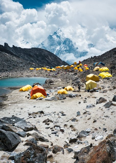 Bunte Zelte am Ufer eines Bergsees, umgeben von felsigen Landschaften und Wolken.