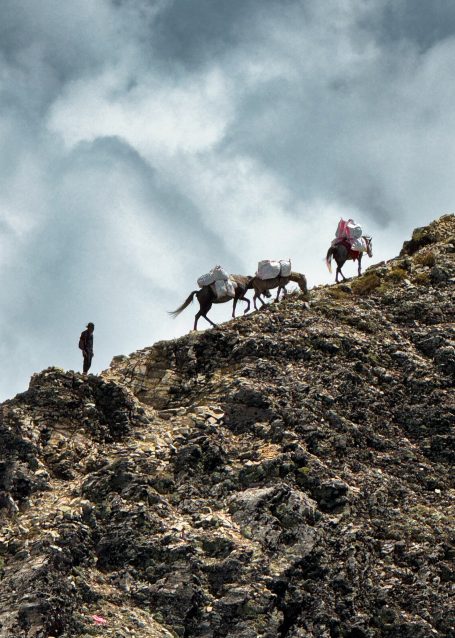 Reiter und Pferde erklimmen einen steilen Berghang unter dramatischen Wolken.