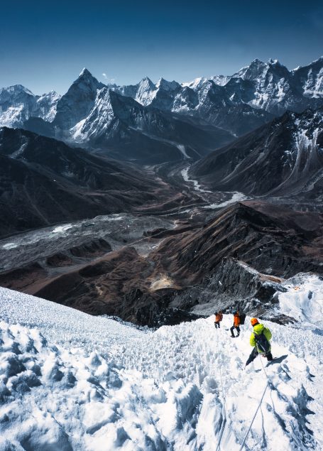 Bergsteiger klettern auf einem schneebedeckten Hang mit Blick auf das Tal und die Berge.