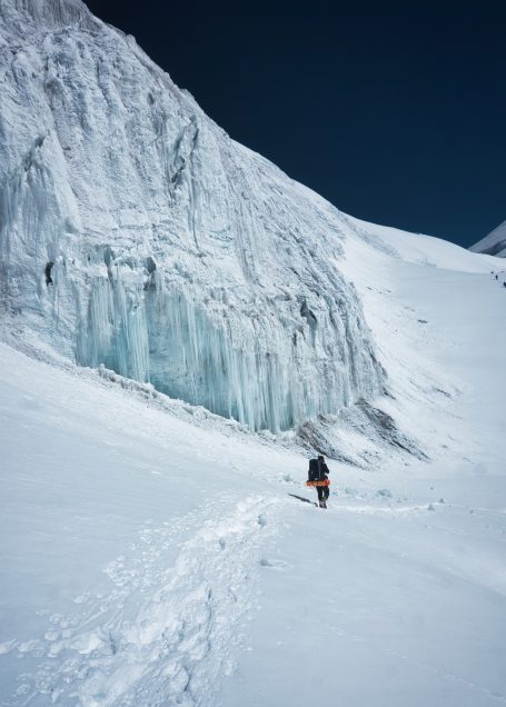 Winterlandschaft mit einem Wanderer, der an einem Gletscher entlanggeht.