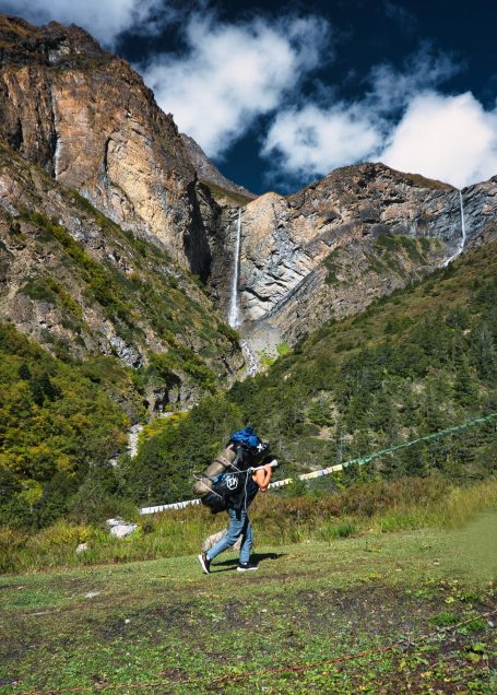 Wanderer mit Ausrüstung in einer bergigen Landschaft mit Wasserfällen im Hintergrund.