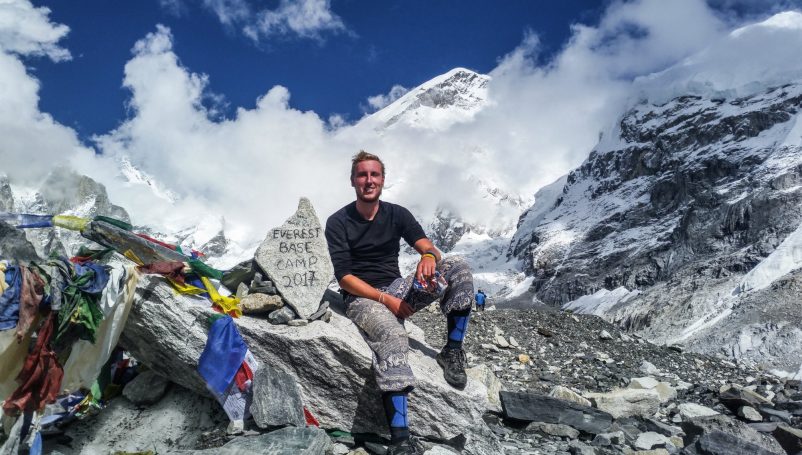 Mann sitzt auf einem Berg mit Aussicht auf schneebedeckte Gipfel und Gebetsfahnen.