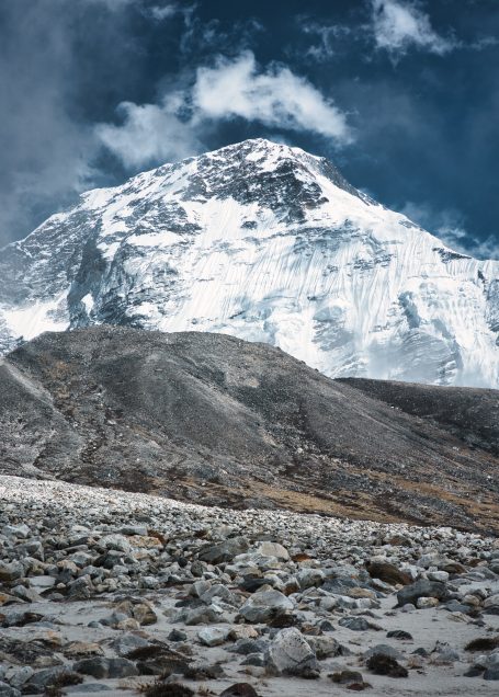 Hoher Berg mit schneebedecktem Gipfel und steiniger Landschaft im Vordergrund.