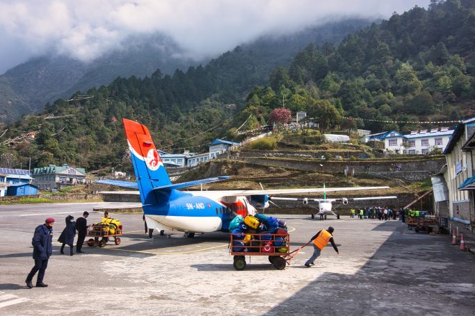 Ein Flughafen in den Bergen mit Flugzeug, Gepäcktransport und Arbeiter auf dem Boden.