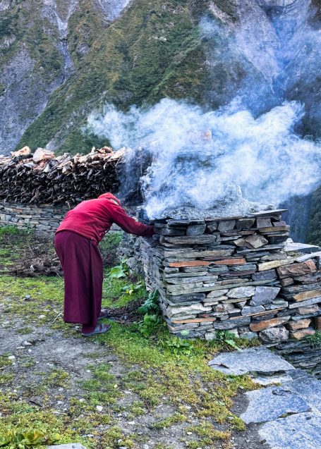 Eine Person in traditioneller Kleidung steht an einem Rauch hüllenden Steinhaufen.