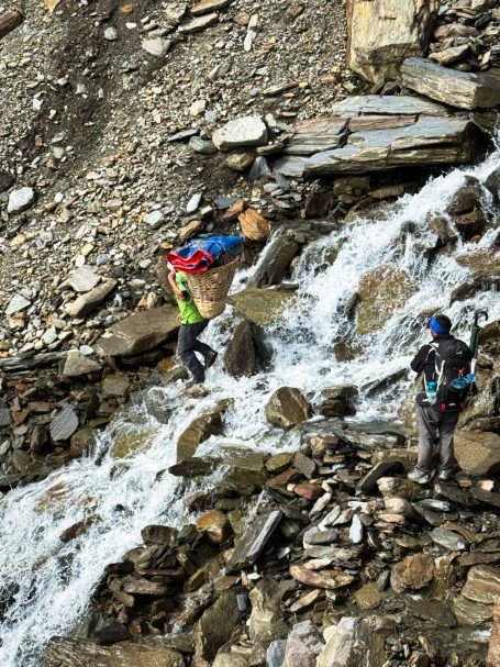 Bergsteiger überqueren einen Wasserfall auf steinigem Terrain.