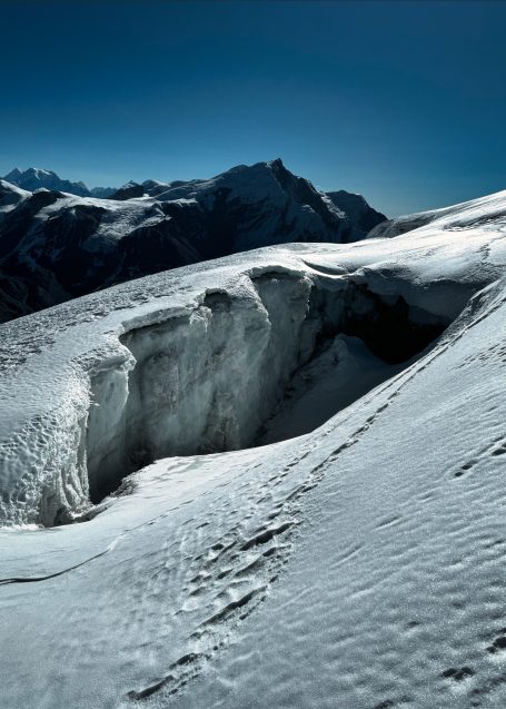 Hochalpinlandschaft mit schneebedeckten Bergen und einer tiefen Gletscherspalte.