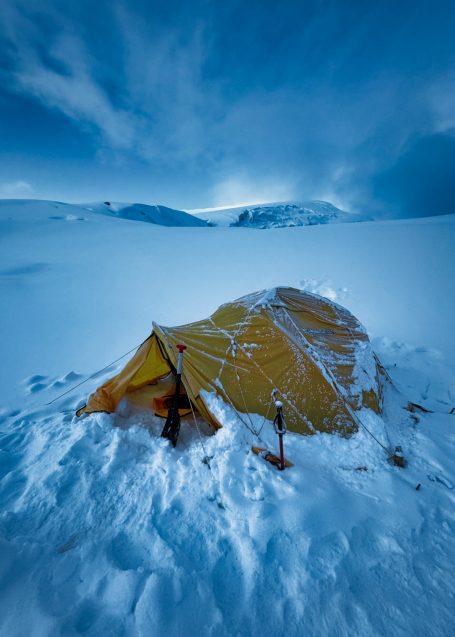 Gelbe Zelt in verschneiter Landschaft unter einem bewölkten Himmel.