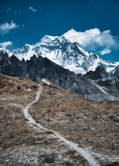 Schneebedeckte Bergspitzen mit klarblauem Himmel und einem schmalen Pfad im Vordergrund.