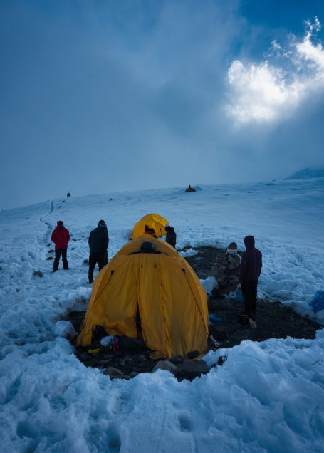 Zelt auf schneebedecktem Boden mit Personen im Hintergrund unter bewölktem Himmel.