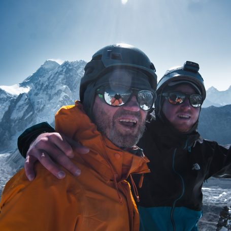 Zwei Männer in Skibekleidung lächeln vor einer Berglandschaft.