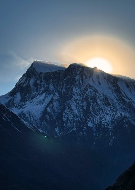 Sonnenaufgang hinter schneebedecktem Berg, diffuse Lichtstrahlen im Hintergrund.