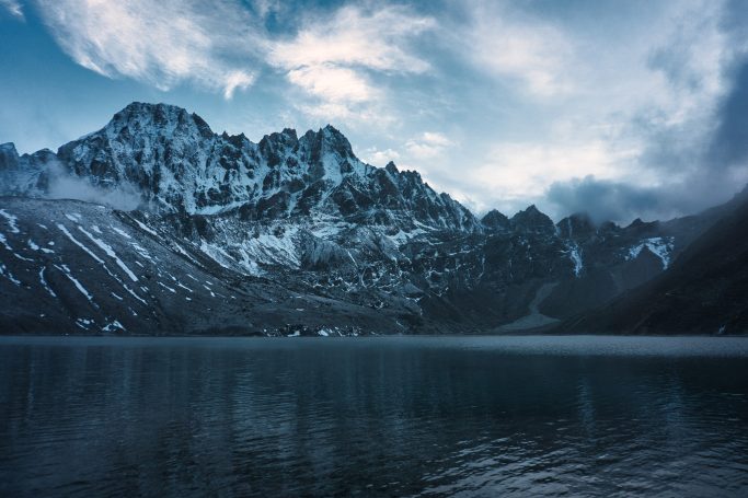 Berglandschaft mit schneebedeckten Gipfeln und ruhigem See im Vordergrund.