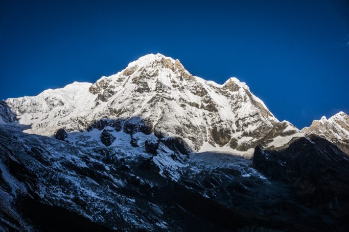 Hoher Berg mit schneebedecktem Gipfel vor einem klaren blauen Himmel.