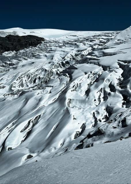 Schneebedeckte Gletscherlandschaft mit tiefen Spalten und klar blauem Himmel.