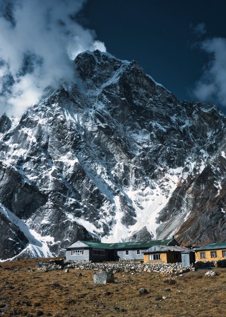 Hohe Berglandschaft mit schneebedecktem Gipfel und traditionellen Hütten im Vordergrund.