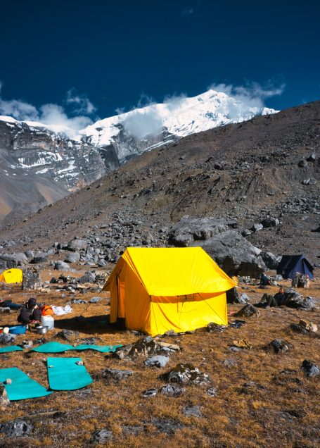 Gelbe Zelt in rauer Gebirgslandschaft mit schneebedeckten Gipfeln.
