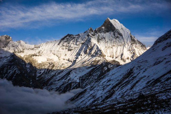 Hoher, schneebedeckter Berggipfel mit dramatischem Wolkenhimmel im Hintergrund.