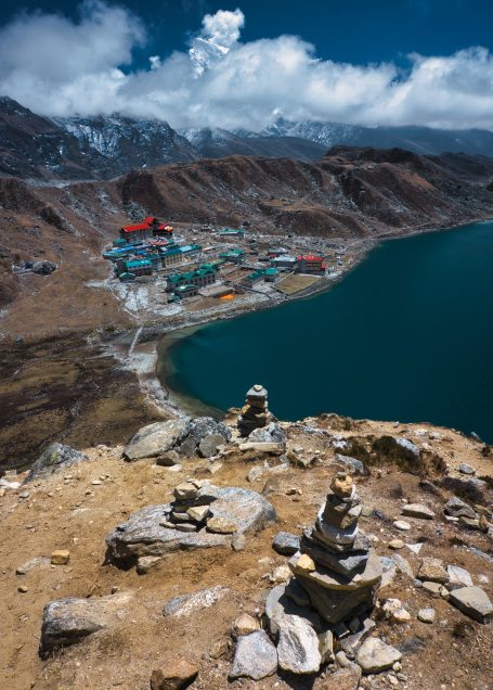 Blick auf einen See und eine Siedlung in den Bergen, umgeben von Felsen und Wolken.