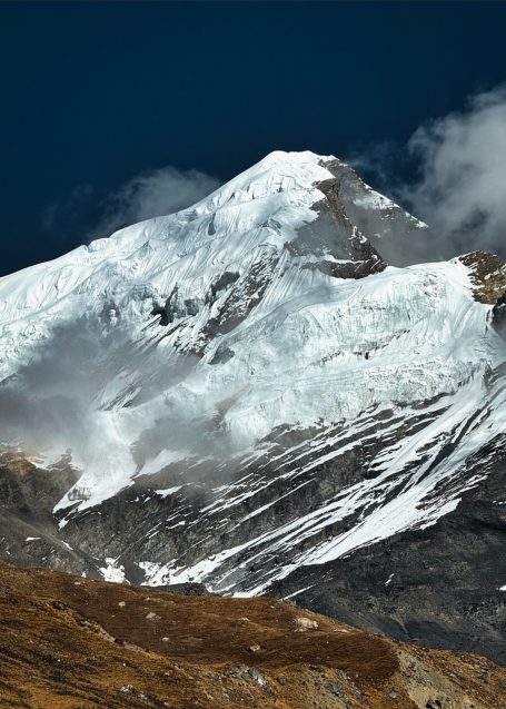 Schneebedeckter Gipfel eines Berges mit Wolken im Hintergrund.