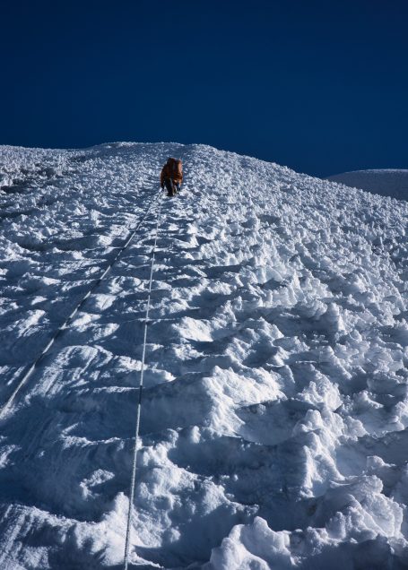 Alpenbesteiger erklimmt eine schneebedeckte Hänge mit klarem Himmel im Hintergrund.