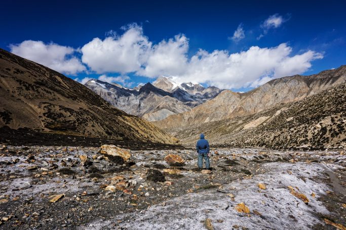 Ein Wanderer in blauer Jacke steht vor einer spektakulären Berglandschaft mit Wolken.