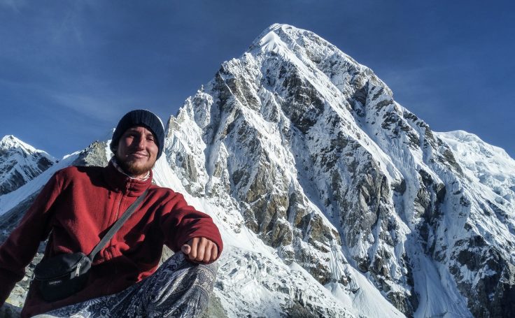 Eine Person in warmer Kleidung posiert vor einem schneebedeckten Berg.