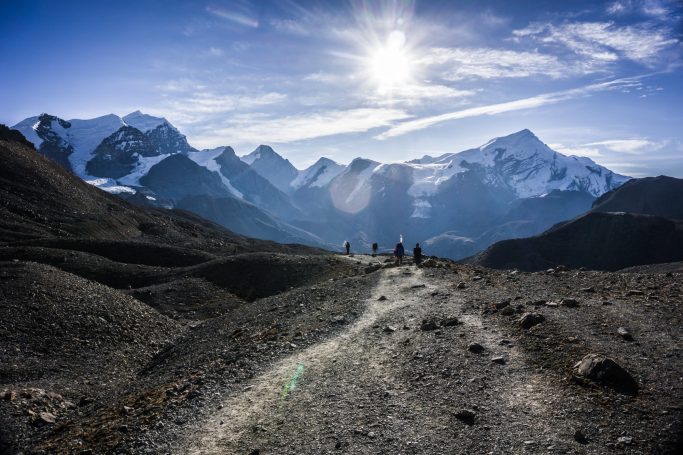 Berglandschaft mit Wanderern auf einem Pfad, umgeben von schneebedeckten Gipfeln.