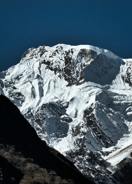 Bedeckter Berggipfel mit Schnee und klar blauem Himmel im Hintergrund.