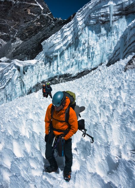 Zwei Bergsteiger in orange und grau erklimmen einen schneebedeckten Gletscher.