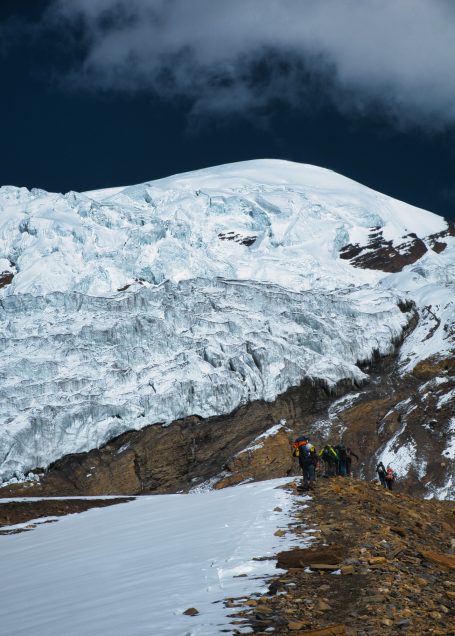 Berglandschaft mit schneebedecktem Gipfel und Wanderern im Vordergrund.