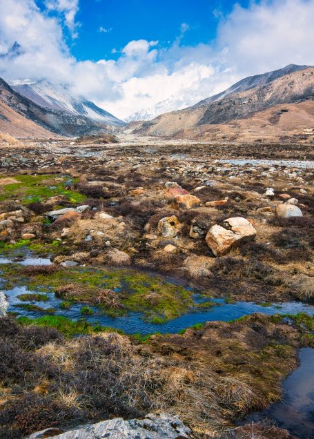 Berglandschaft mit grünen Flächen, Steinen und bewölktem Himmel.