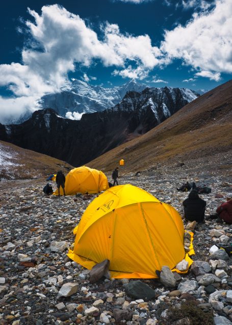 Gelbe Zelte auf steinigem Gelände mit dramatischem Bergpanorama im Hintergrund.